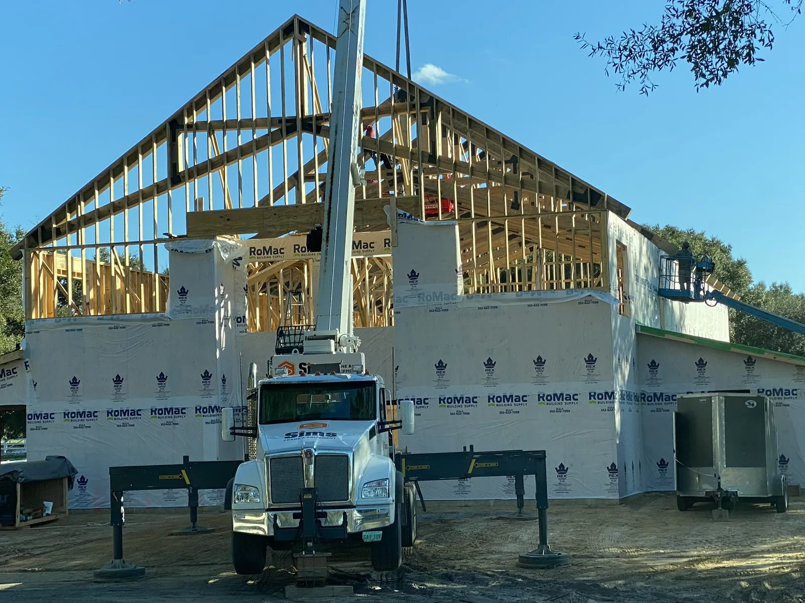 Crane truck setting roof trusses on a framed home wrapped in house wrap