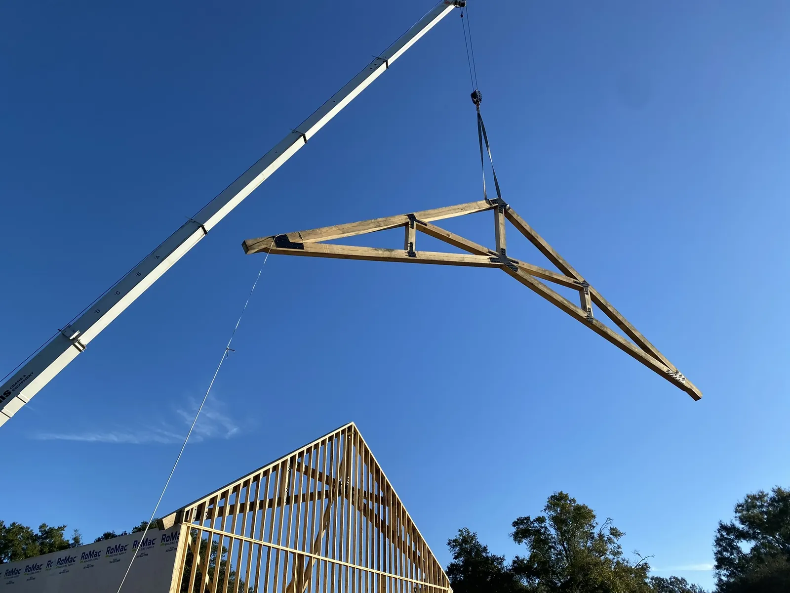 Crane lifting a wood roof truss into place above a framed home