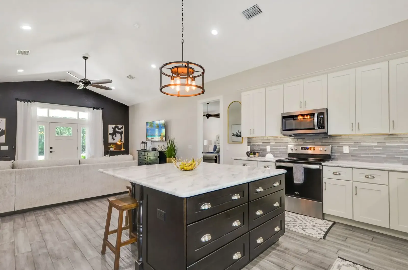 Kitchen with white cabinets, a dark island and an industrial pendant light