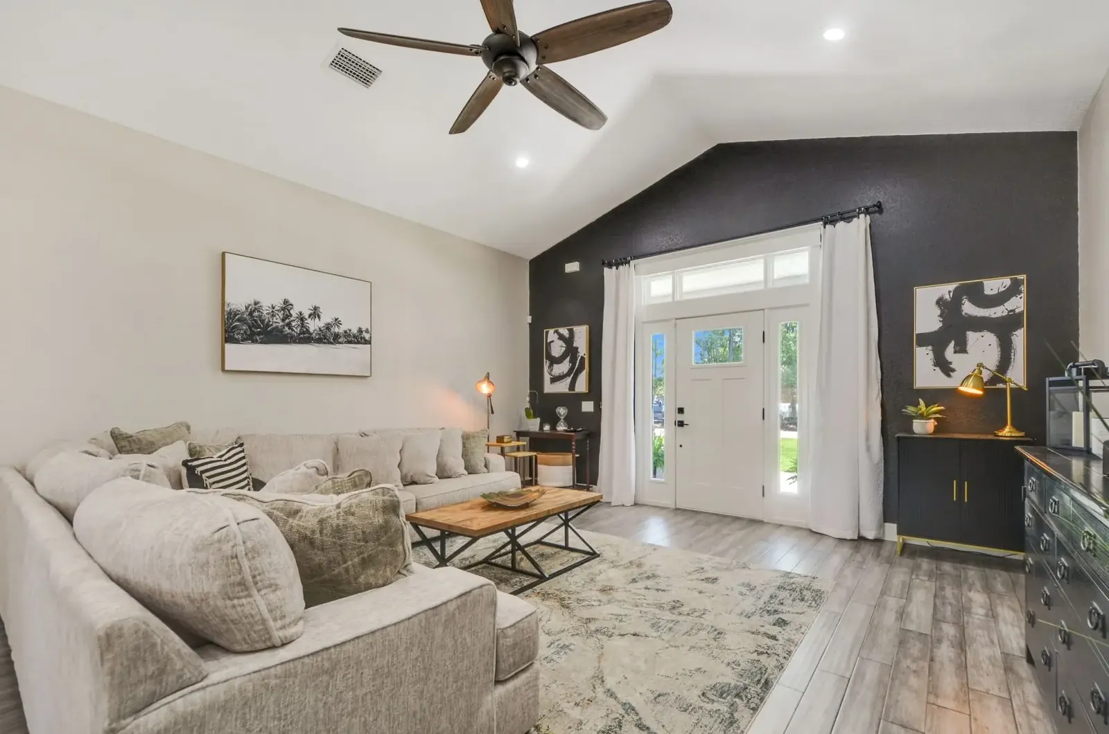 Living room with a vaulted ceiling, sectional sofa and a dark accent wall by the front door
