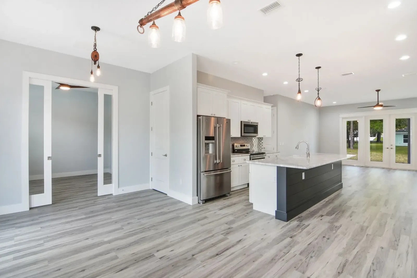 Open kitchen and great room with white cabinets, a dark island and wood-look plank flooring