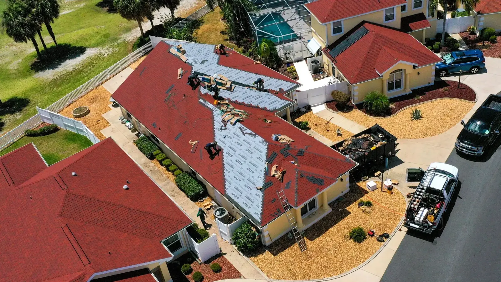 Aerial view of a roof replacement in progress with a dumpster and work truck beside the house