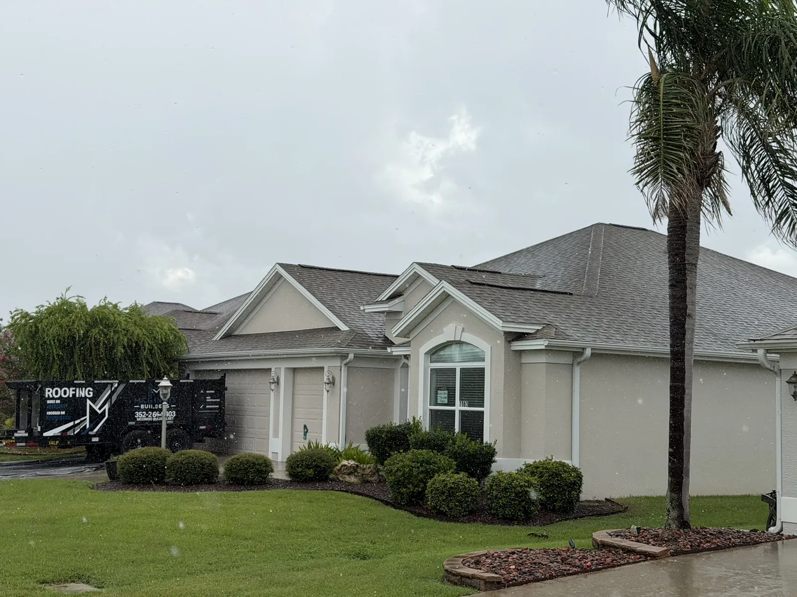 Home with a new shingle roof and a McGinnis Builders roofing trailer out front